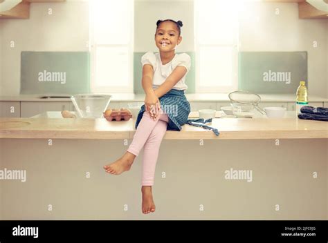 Portrait Of A Cute Young Mixed Race Girl Sitting On The Kitchen Counter With An Apron And