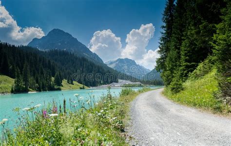 Summer Mountain Landscape With Turquoise Lake And Gravel Road Bordered