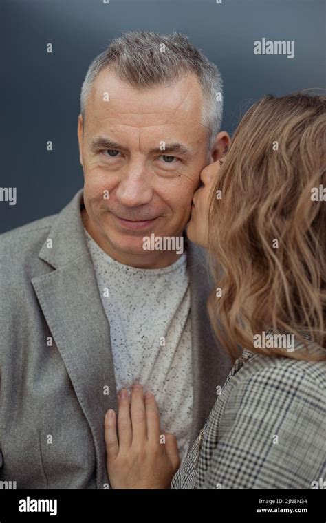 Young Loving Woman Gently Kissing Handsome Aged Gray Haired Partner