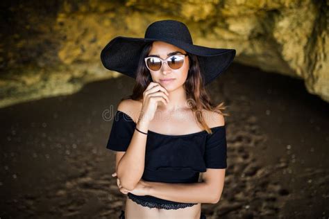 beautiful latin woman thinking with hat and sunglasses sunbathing on rocks beach on summer