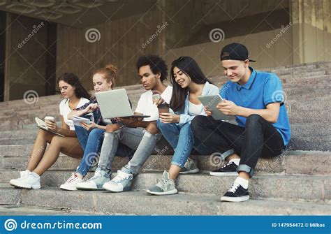 Group Of Diverse Teenagers Using Gadgets Sitting On Stairs Outdoor