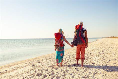 Couple Of Travelers With Backpacks Stands On A Deserted Beach Stock