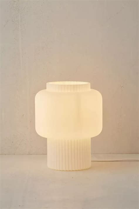 A White Table Lamp Sitting On Top Of A Floor Next To A Wall And Window
