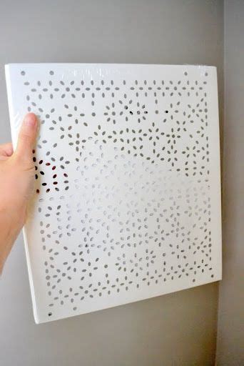 A Persons Hand Is Pointing At A White Wall Panel With Holes On It