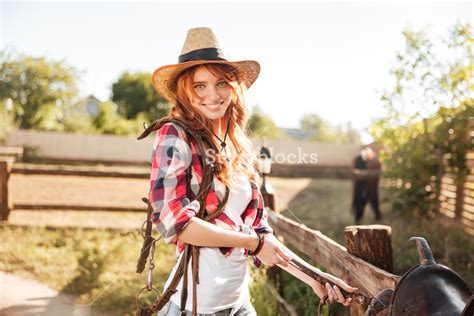 Happy Redhead Young Woman Cowgirl Preparing Saddle For Riding Horse