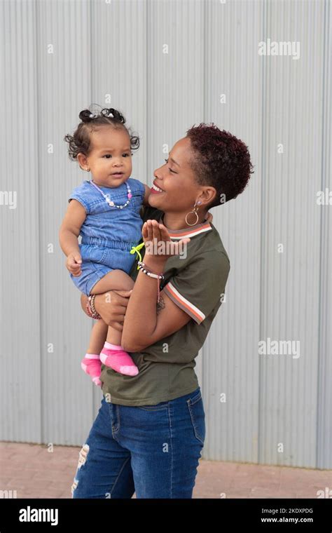 Smiling Colombian Mom Holding Embracing Cute Baby Daughter Against Gray