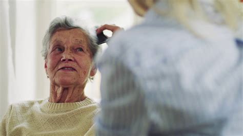 A Young Health Visitor Combing Hair Of Senior Woman At Home Stock