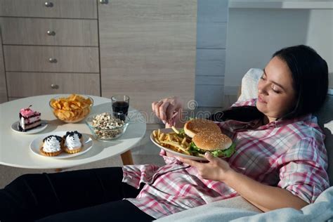 Happy Overweight Woman Eating French Fries With Burgers At Home Stock