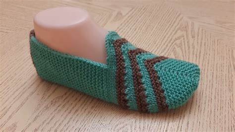 A Green Knitted Slipper Sitting On Top Of A Wooden Floor Next To A Bottle