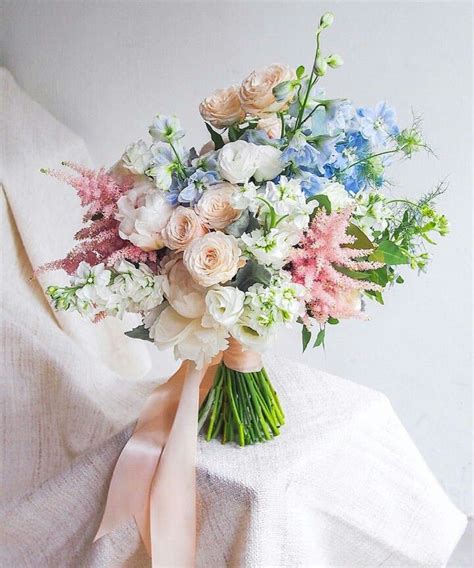 A Bridal Bouquet With Pink White And Blue Flowers On A Bed Sheet In