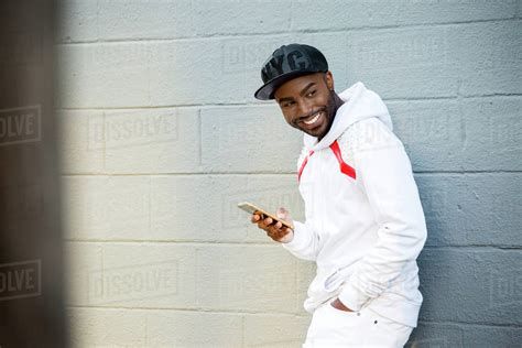 Smiling Black Man Leaning On Wall Holding Cell Phone Stock Photo