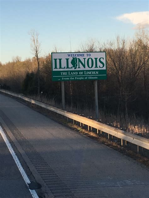 A Welcome To Illinois Sign On The Side Of A Road With Trees In The