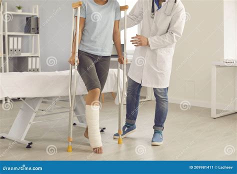 Patient With Broken Leg Walking With Crutches Assisted By Doctor During