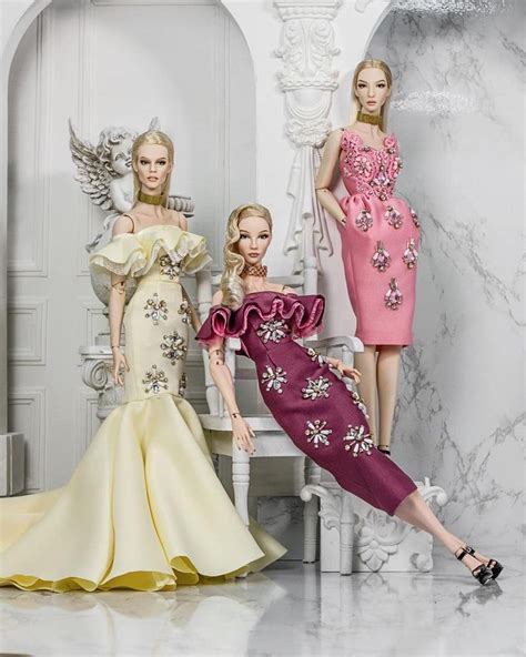 Three Barbie Dolls Are Posed In Front Of A White Marbled Room With An Arch