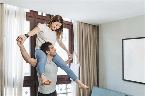 Playful Man Carrying Woman On Shoulders In Hotel Room Stock Photo