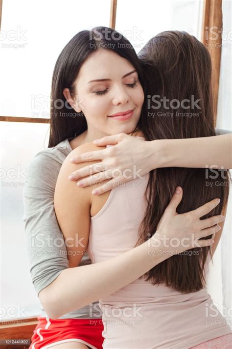 Lesbian Couple In Bedroom At Home Standing One Woman Sitting On Sill