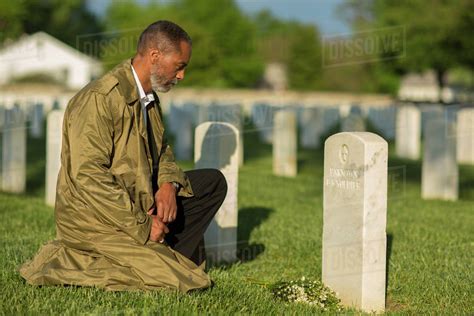 Black Man Kneeling With Bouquet At Military Cemetery Stock Photo