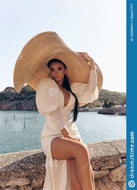 Beautiful Woman With Dark Hair In Luxurious White Dress And Hat Posing In Beautiful Landscape