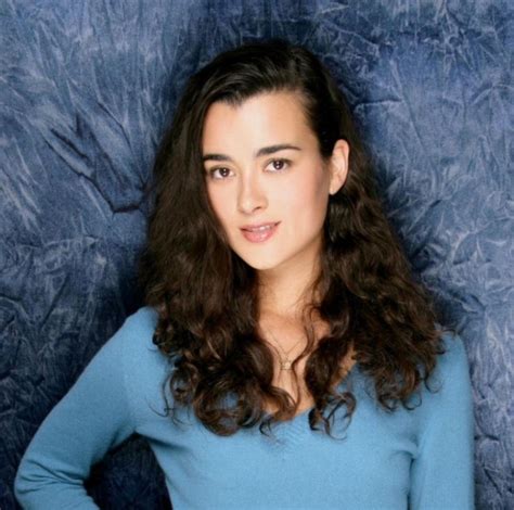 A Woman With Long Dark Hair And Blue Shirt Posing In Front Of A Black
