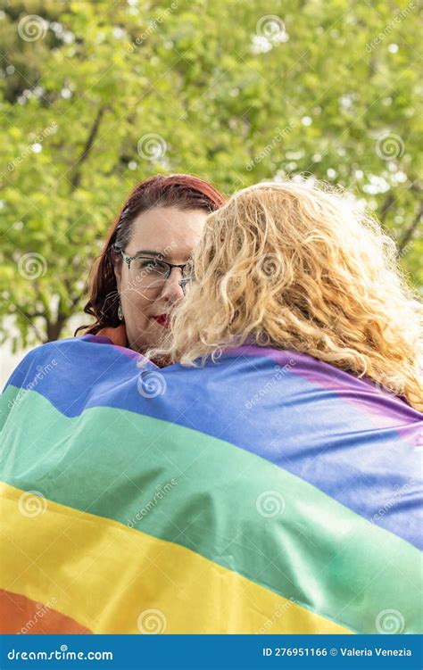 Lesbian Couple Embracing Under Lgbt Rainbow Flag One Of Them Is Looking At Camera Concept Of