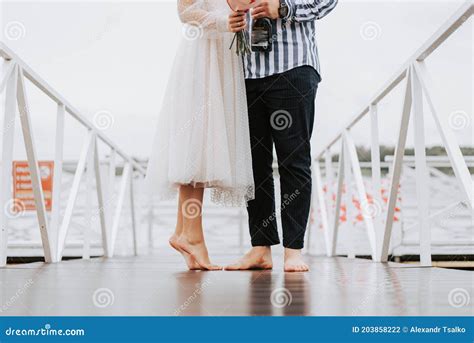 Groom With The Barefoot Bride Walk Holding Hands Along The Pier On The