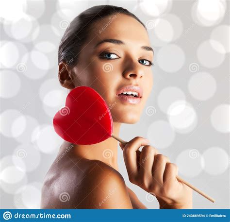 Attractive Model With Tanned Skin Holds A Red Heart Shaped Lollipop In