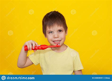 Happy Toddler Boy Brushing His Teeth With A Toothbrush On A Yellow