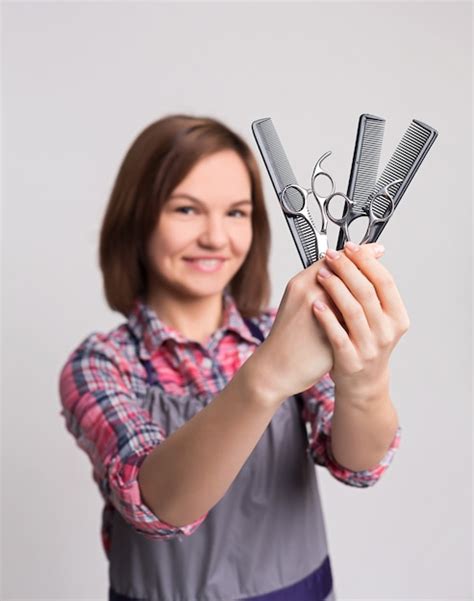 Premium Photo Smiling Woman Holding Scissors And Combs At Gray Studio