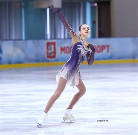 A Female Figure Skating On An Ice Rink In A Purple And White Outfit