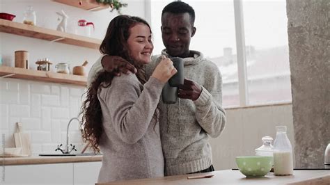 Interracial Couple Drinking And Hugging In Kitchen By Stocksy