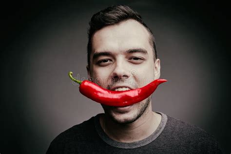 man holding chili pepper in his teeth funny guy eating hot spicy pepper on a gray background