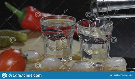 Pour Vodka From A Bottle Into Shot Glasses With Ice Cubes On The Table