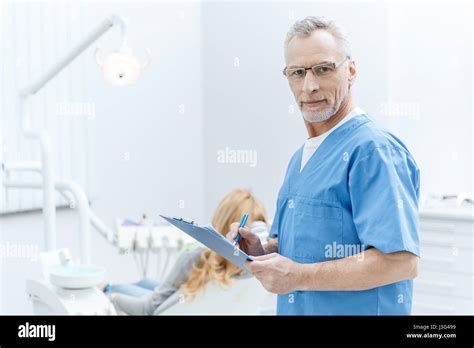 Senior Dentist In Uniform Writing On Clipboard In Dental Clinic With