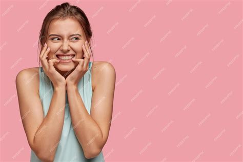 Free Photo Photo Of Cheerful Content Young Woman With Pleasant Smile Keeps Hands On Face