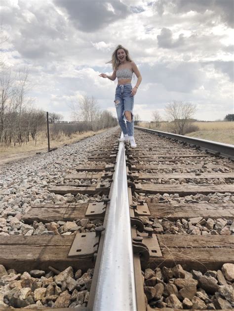A Woman Standing On The Railroad Tracks With Her Arms Out And Looking At The Camera