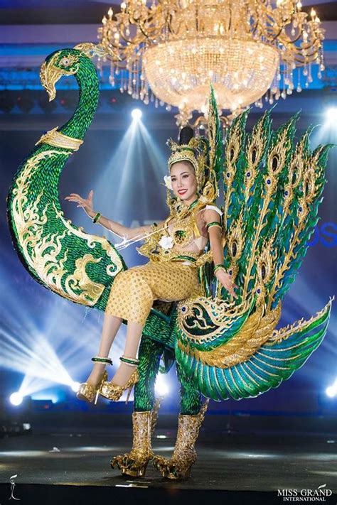 A Woman Dressed In Green And Gold Dancing With A Peacock Costume On Her Back