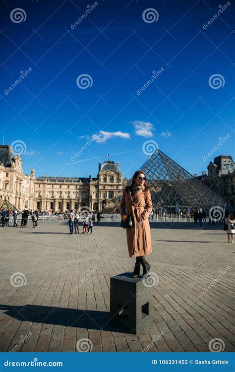 A Young Girl In A Brown Coat And Scarf Stands On The Background Of The