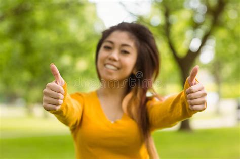 Female College Student With Books Gesturing Thumbs Up In Park Stock