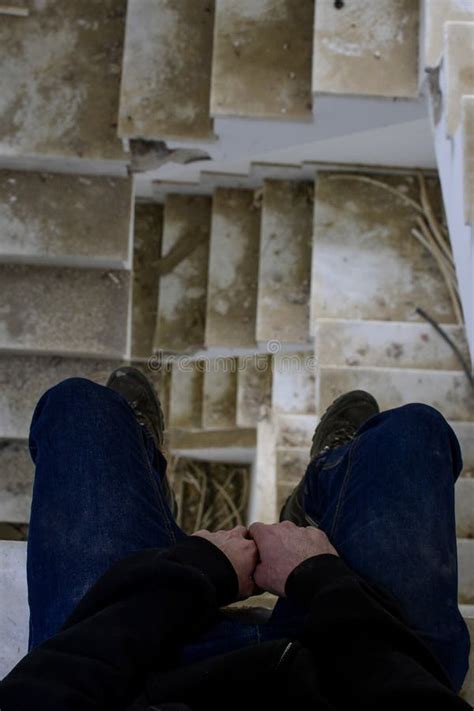 Vertical Shot Of A Man Sitting In The Ruined Staircase Of An Abandoned