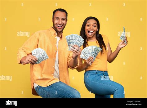 Excited Young African American Couple Holding Money Dancing And Celebrating Big Win On Yellow