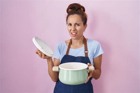 brunette woman wearing apron holding cooking pot clueless and confused expression stock image