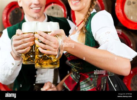 Young Couple Man And Woman In Traditional Bavarian Tracht Drinking Beer In A Brewery In Front
