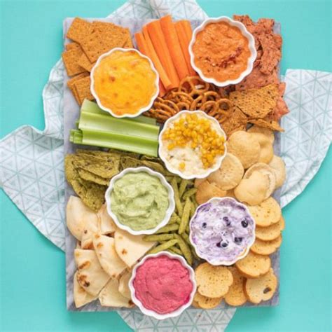 A Platter Filled With Crackers Dips And Veggies On A Blue Background