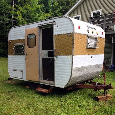 An Old Camper Trailer Is Parked In Front Of A House With Siding On It