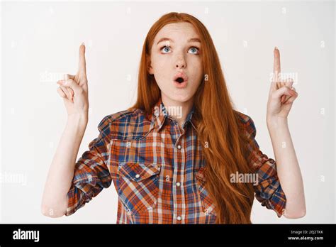 Portrait Of Amazed Redhead Girl Pointing Fingers Up Looking At Logo