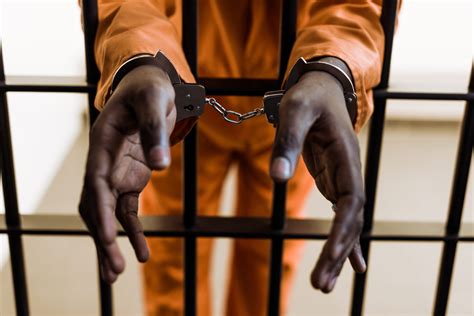 Cropped Image Of African American Prisoner In Handcuffs Behind Prison Bars