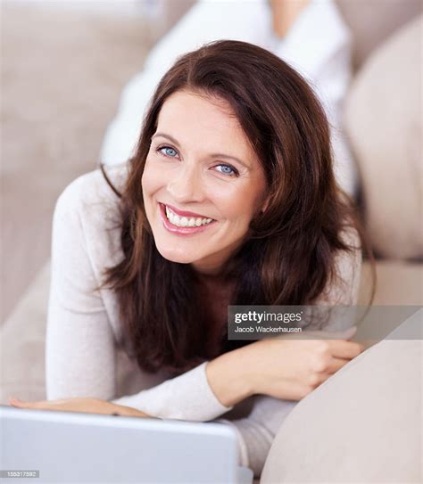 Smiling Mature Lady Lying On Couch And Using Laptop Bildbanksbilder