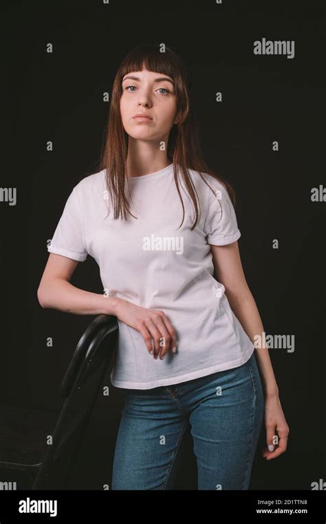 Studio Portrait Of A Pretty Brunette Woman In A White Blank T Shirt Against A Plain Black