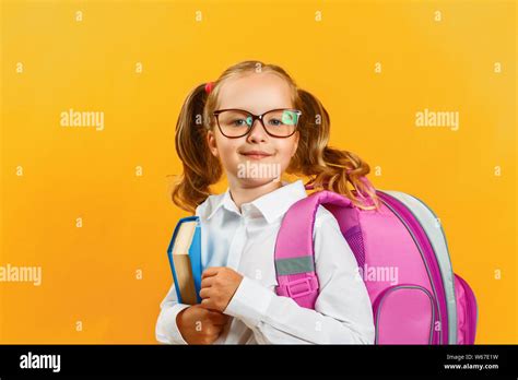 Portrait Of Little Girl Schoolgirl With Backpack And Book On Yellow