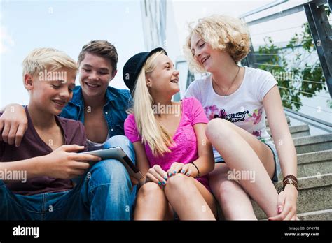 Group Of Teenagers Sitting On Stairs Outdoors Looking At Tablet